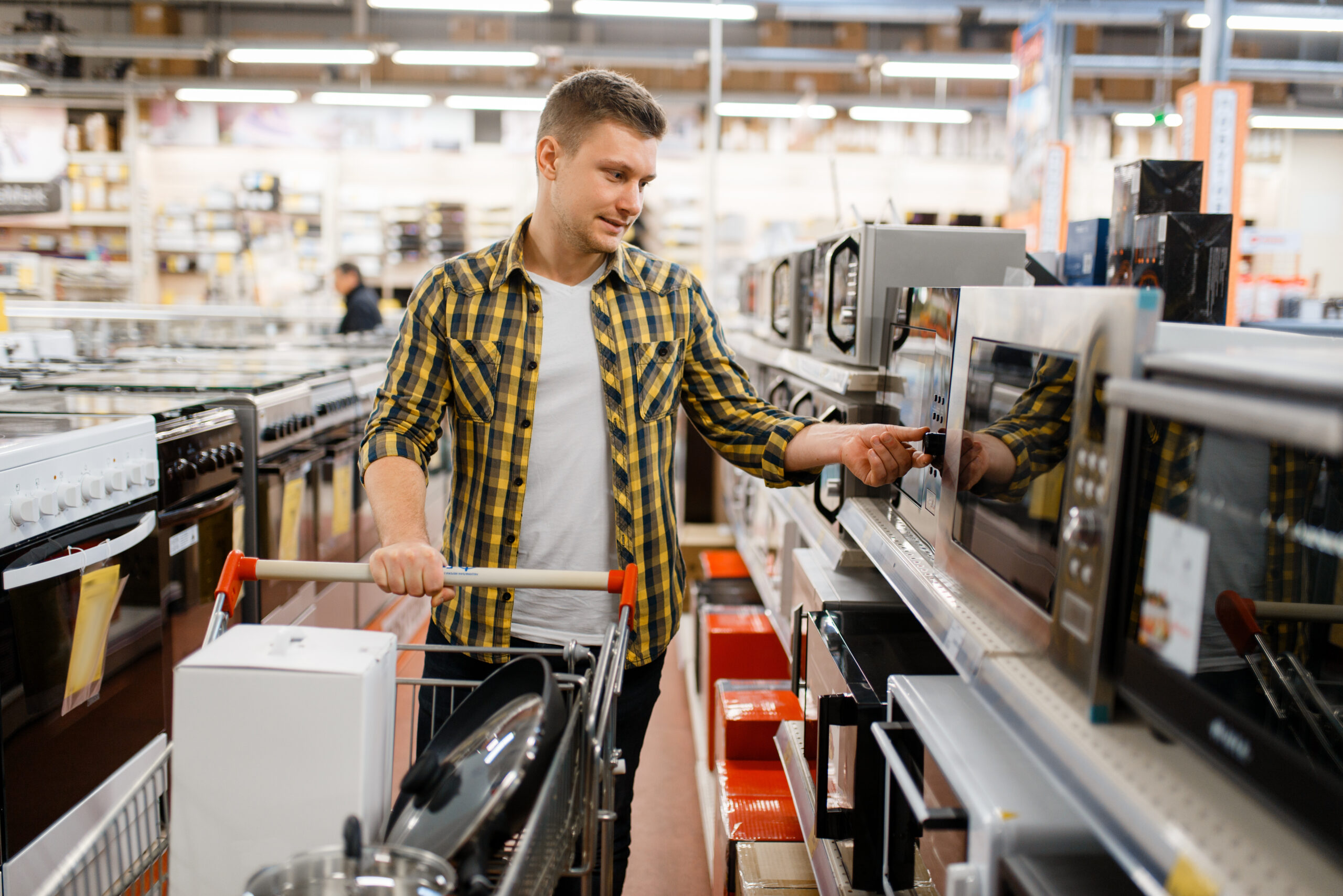 Un homme regarde les micro-ondes en rayon dans un magasin, et pousse son caddie.