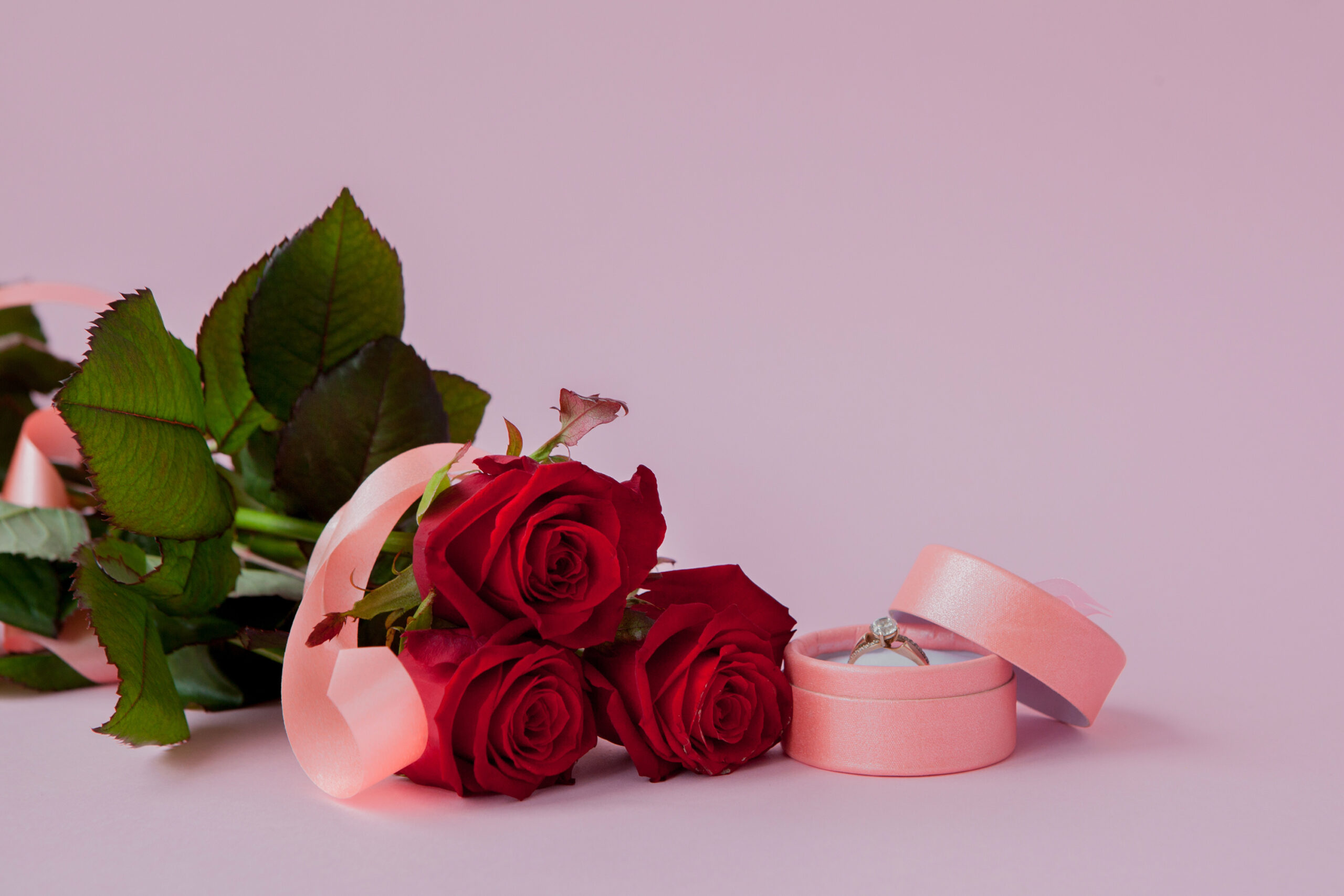 Un bague dans un écrin à côté d'un bouquet de roses rouges
