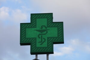 Green cross of a pharmacy in France against a blue sky