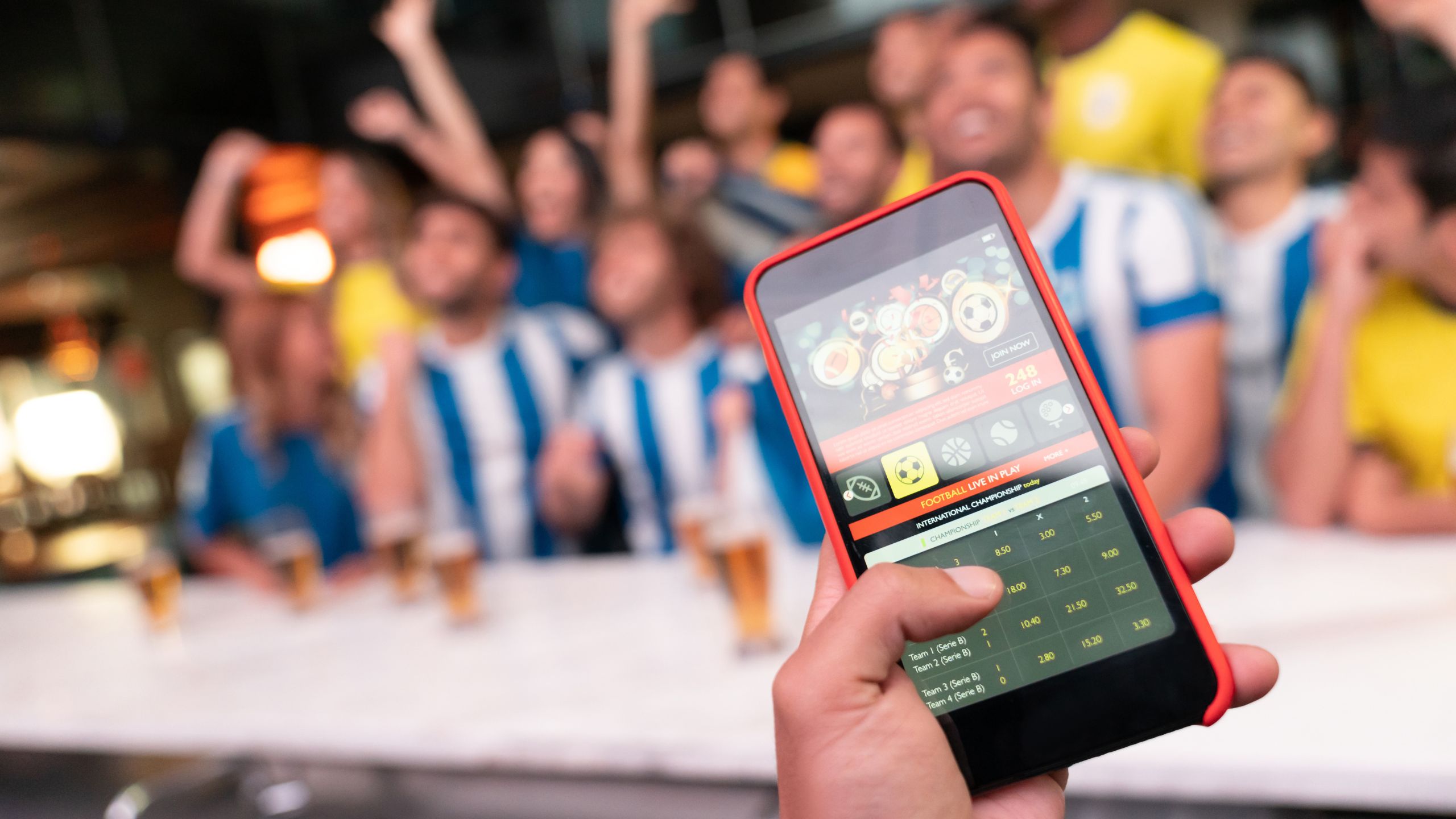 Une main fixe des paris sur un téléphone avec en fond des supporters