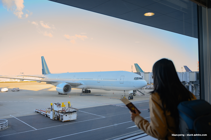 A woman at the airport is looking at a plane through the window
