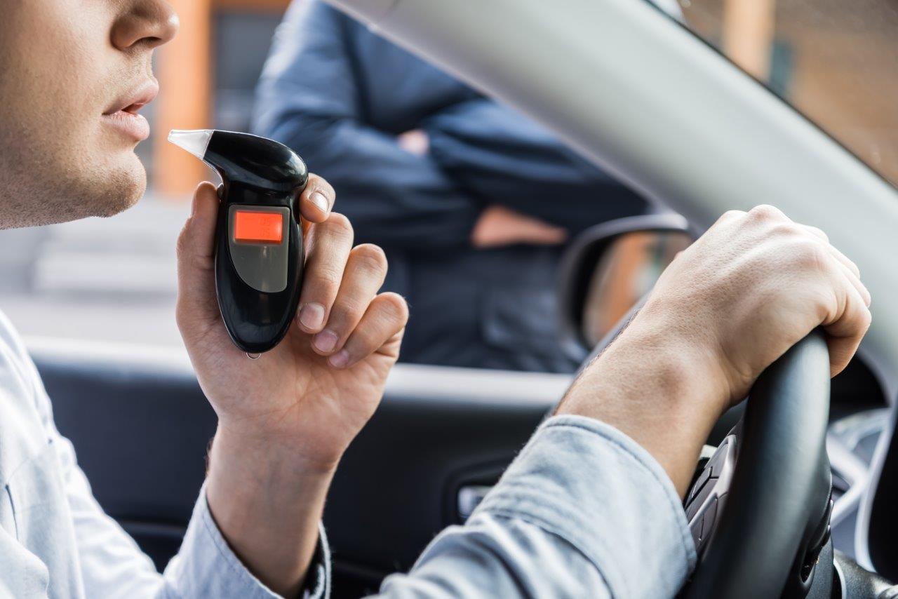 A man blowing in a breathalyser behind the wheel of his car