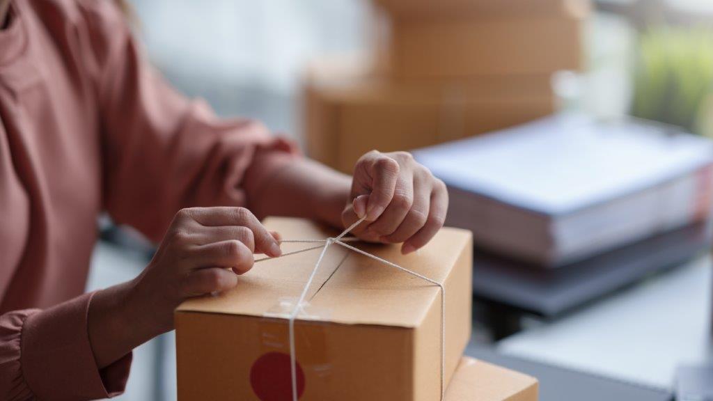 A person is closing a parcel using a piece of rope