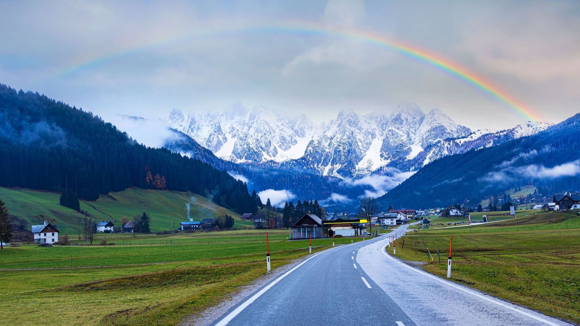 a road with snow-capped mountains and a rainbow