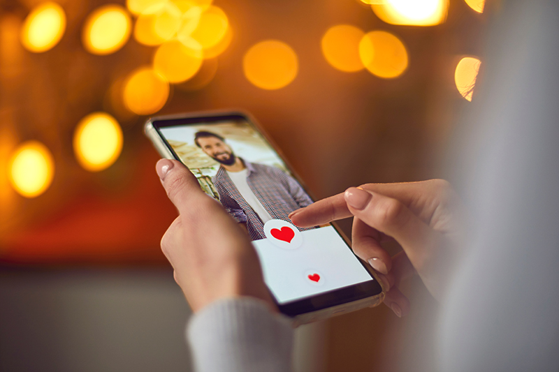 Une femme regarde la photo de profil d'un jeune homme séduisant sur une application de rencontre et appuie sur le bouton « J'aime » en forme de cœur rouge. Gros plan sur les mains d'une femme tenant un téléphone portable.