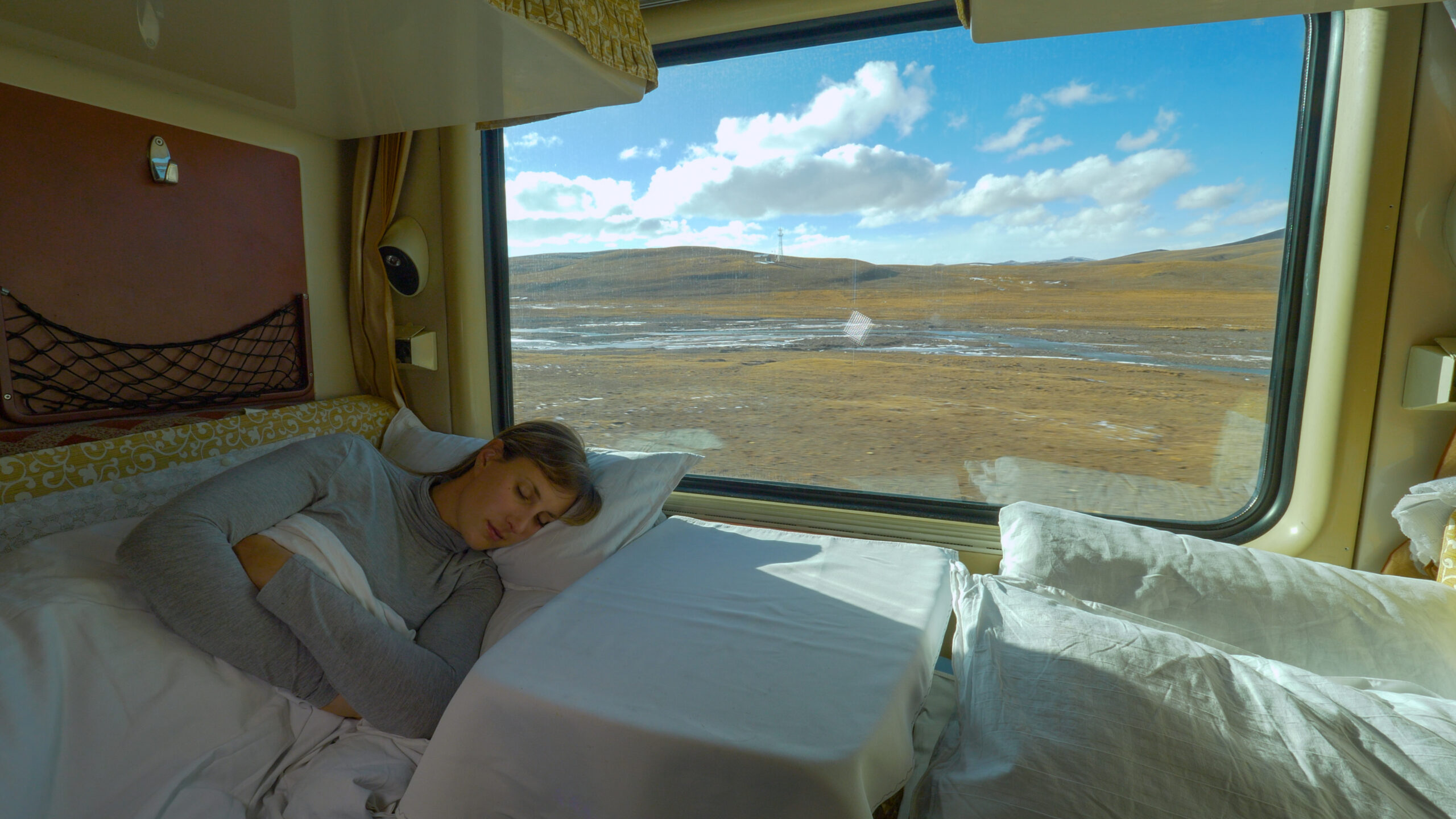 Une femme dort paisiblement à l'intérieur d'un train de nuit pendant que le paysage de steppe défile à l'extérieur, par la fenêtre