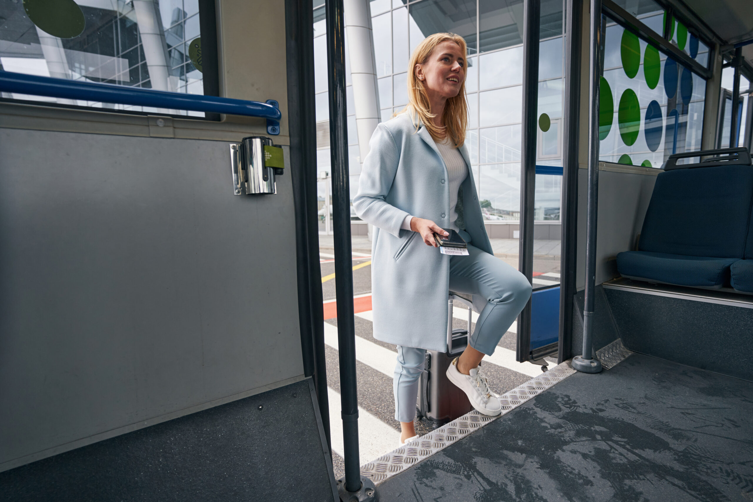 A woman boards a shuttle bus at the airport, her plane ticket in one hand and her suitcase in the other.