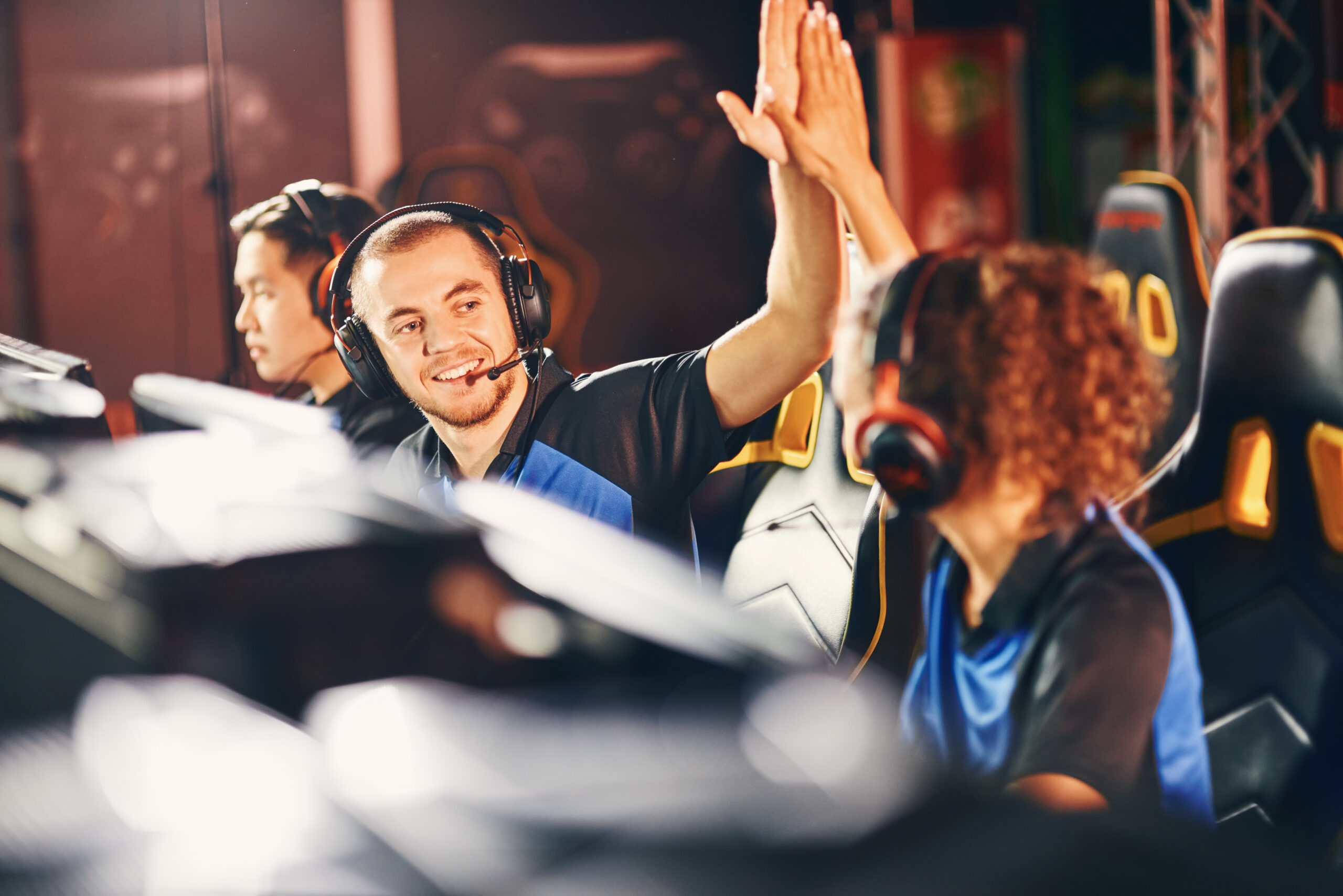 Two young happy professional cyber sport gamers giving high five to each other, celebrating success while participating in eSports tournament. Playing online video games professionally