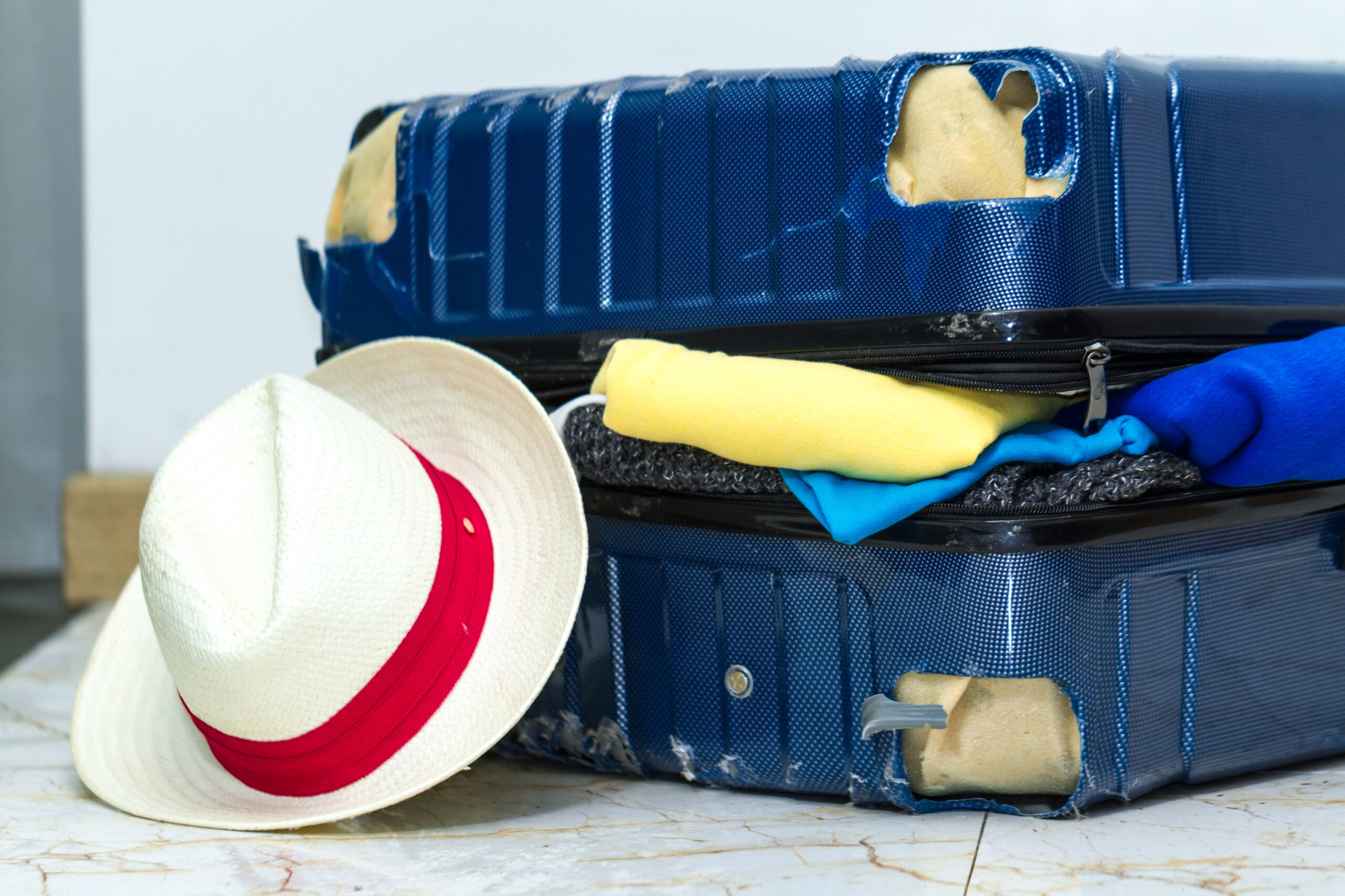 Gros plan sur une valise endommagée et un chapeau de paille posé contre la valise
