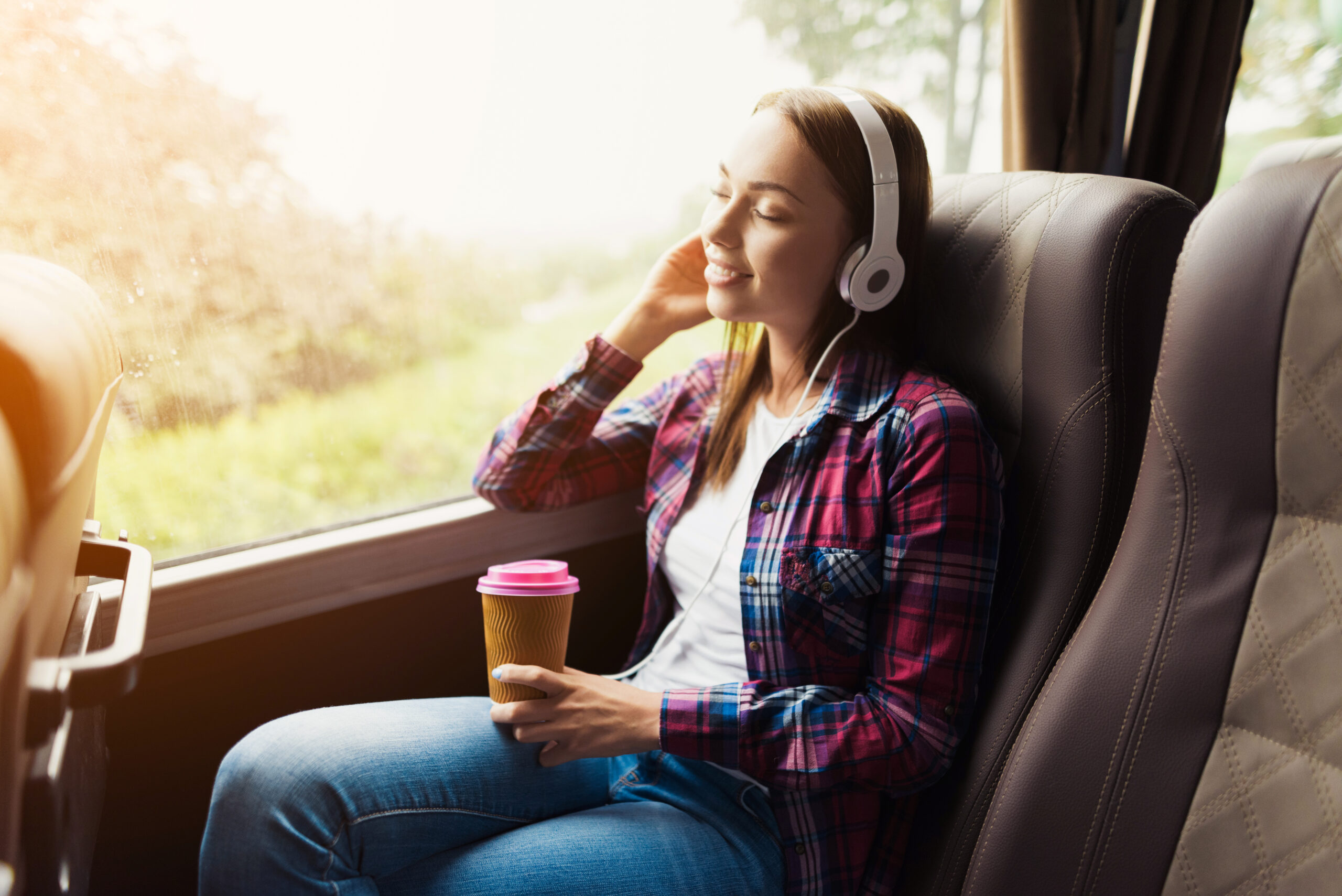 Une jeune femme est assise dans le train, un gobelet de café à la main, et écoute de la musique