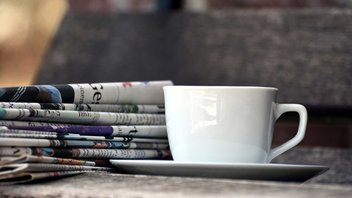 Gros plan sur une tasse de café avec une pile de journaux en arrière-plan.
