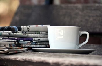 Gros plan sur une tasse de café avec une pile de journaux en arrière-plan.