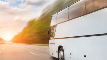Un bus blanc roule sur l'autoroute, sur fond d'un coucher de soleil