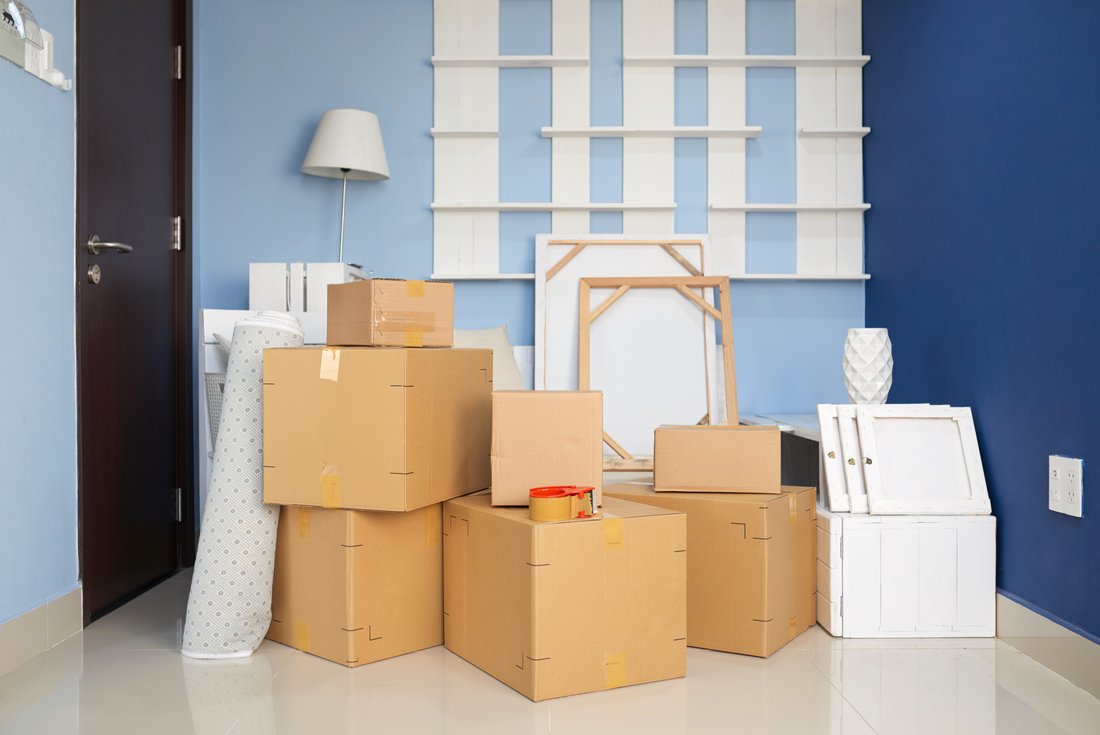 Moving boxes and decorative objects are stacked in a room with blue walls.