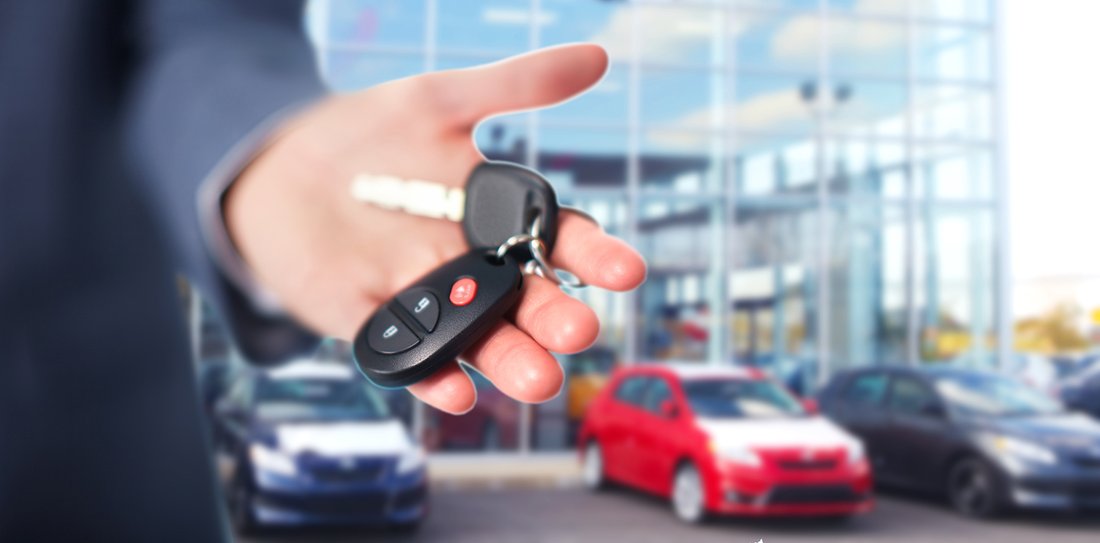 Close-up on a hand showing car keys, with vehicles lined up in the background.