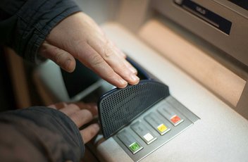 Une personne est en train de cacher le pavé numérique sur le distributeur de billet pendant qu'elle compose son numéro.
