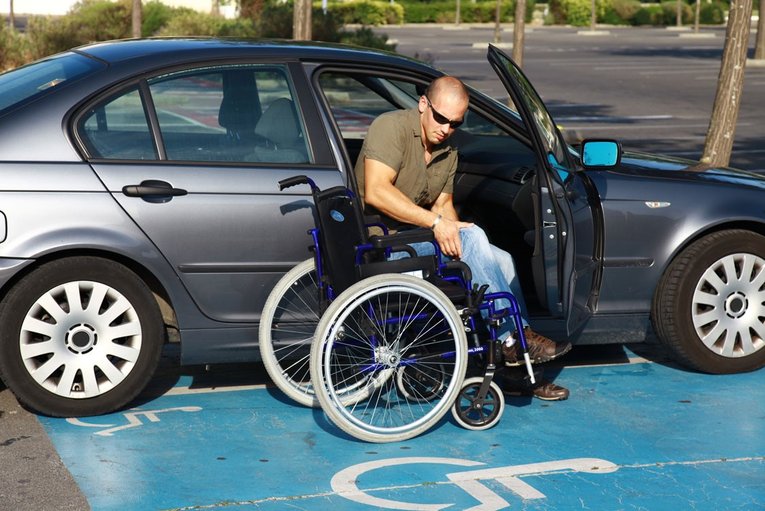 A man in a wheelchair gets out of the car
