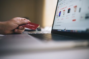 Une personne est devant son ordinateur, sur un site de e-commerce, et tient dans sa main une carte de crédit.