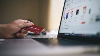 Une personne est devant son ordinateur, sur un site de e-commerce, et tient dans sa main une carte de crédit.