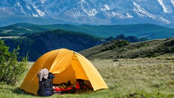 Une tente est installée dans la nature, avec des montagnes en arrière plan.
