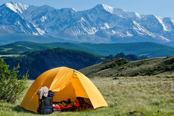 A tent is set up in the nature, with mountains in the background.