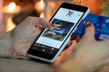 A woman makes an online purchase on her smartphone, and holds her credit card with her right hand to make the payment.