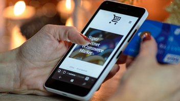 Une femme fait un achat en ligne sur son smartphone, et tient sa carte de crédit avec sa main droite afin de procéder au règlement.