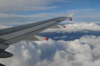View of the wing of an airplane in full flight with clouds in the background.