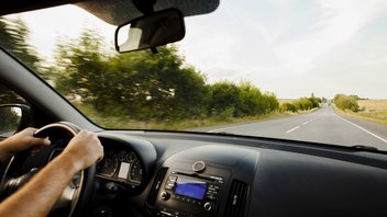 A person at the wheel of his car on an empty country road.