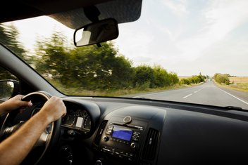 Une personne au volant de sa voiture sur une route de campagne vide.
