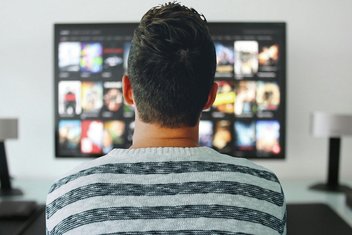 A man, seen from behind looking at a TV screen.