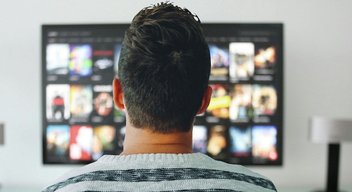 A man, seen from behind looking at a TV screen.