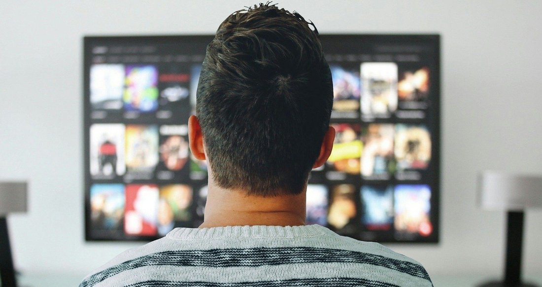 Un homme, vu de dos qui regarde un écran de télévision.