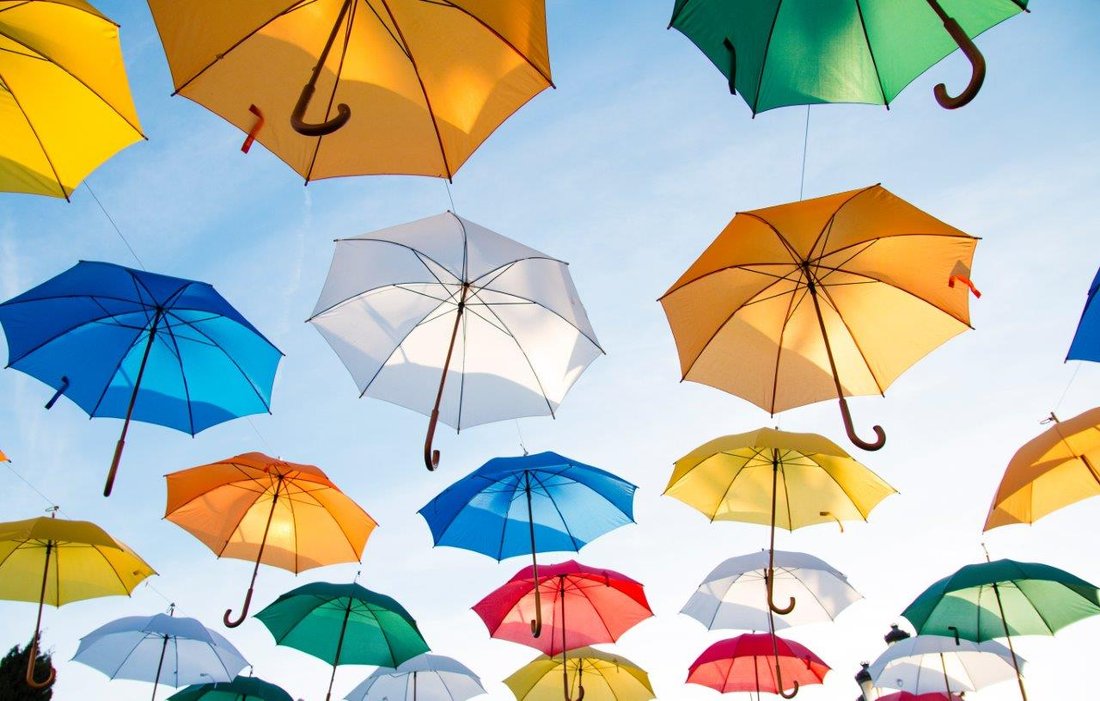 Colourful umbrellas are suspended open to a blue sky in the background.