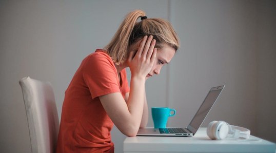 Femme assise devant un ordinateur portable se tenant la tête 