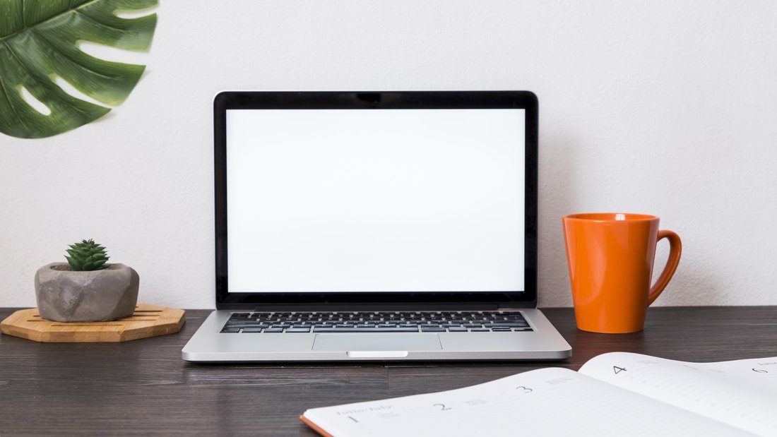 Vue sur un espace de travail avec un ordinateur portable, un agenda, une tasse.