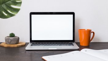 Vue sur un espace de travail avec un ordinateur portable, un agenda, une tasse.