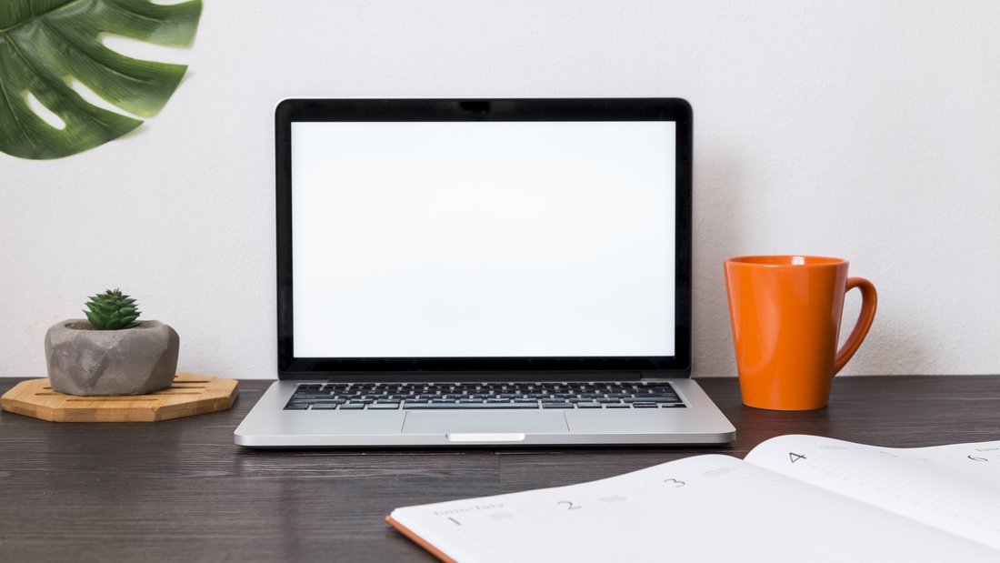 Vue sur un espace de travail avec un ordinateur portable, un agenda, une tasse.