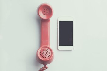 A smartphone is placed next to a vintage phone with pink wire.