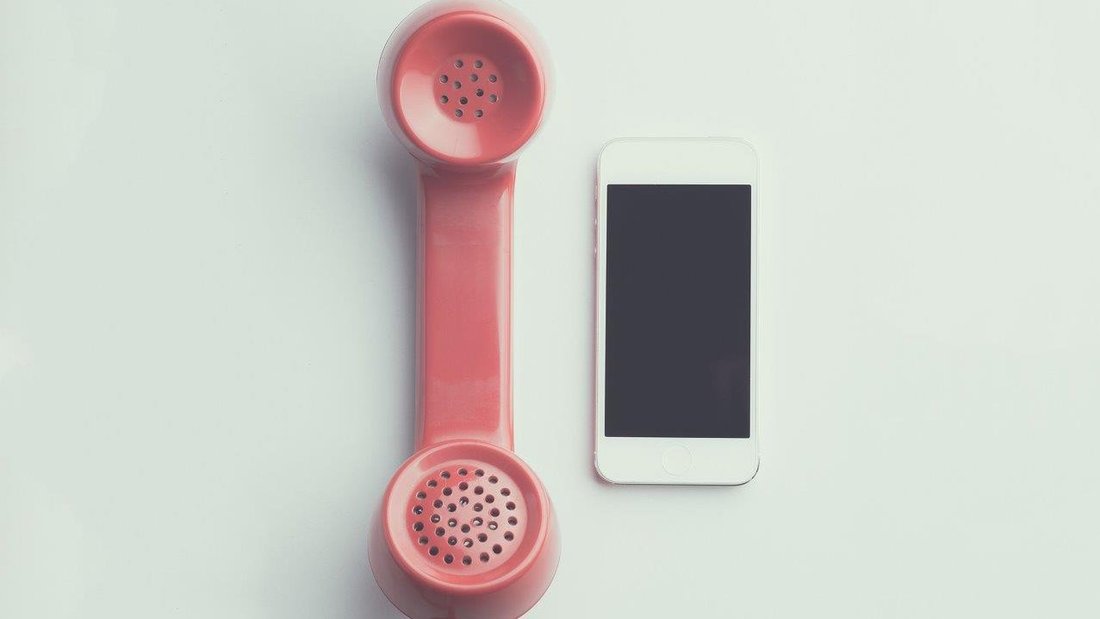 A smartphone is placed next to a vintage phone with pink wire.