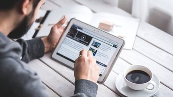 Un homme navigue sur sa tablette, une tasse de café à côté de lui.