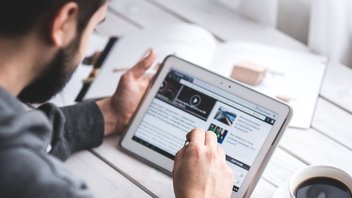 Un homme navigue sur sa tablette, une tasse de café à côté de lui.
