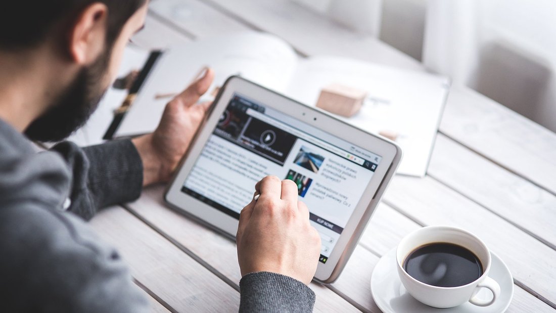 Un homme navigue sur sa tablette, une tasse de café à côté de lui.